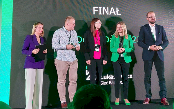 grupa ludzi na scenie przed ciemnym banerem